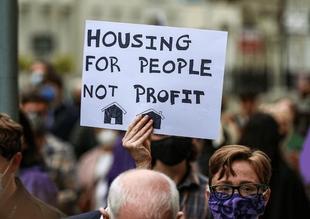 A woman protesting with a billboard which says "Housing for people not for profit"