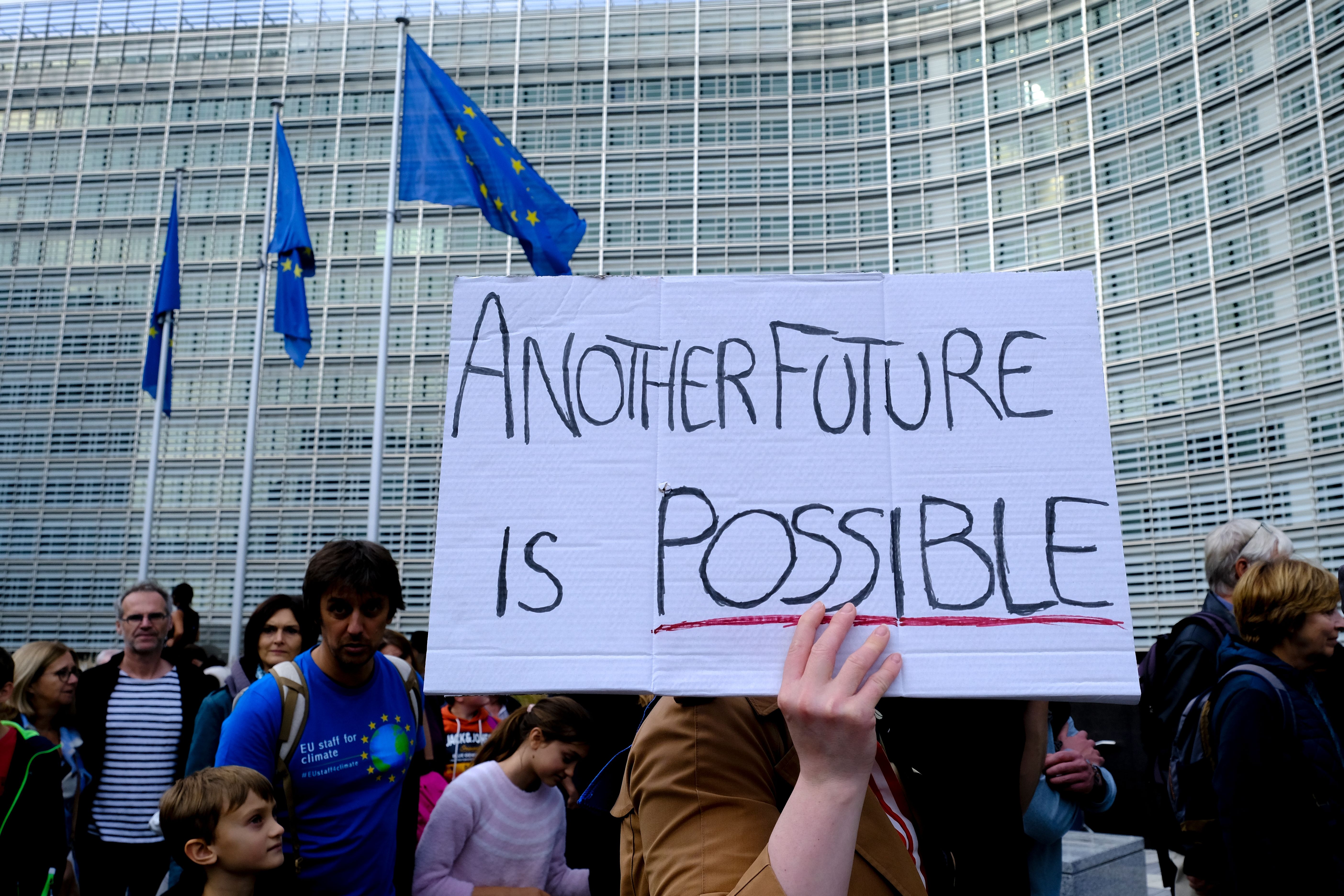 Poster di una manifestazione di fronte alla commissione europea con su scritto "Un altro futuro è possibile"